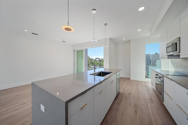 kitchen featuring appliances with stainless steel finishes, sink, light hardwood / wood-style flooring, hanging light fixtures, and a large island