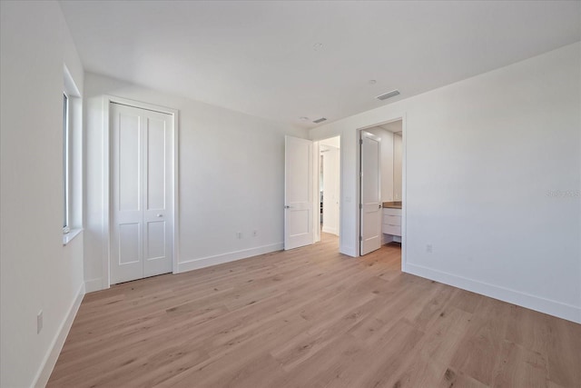 unfurnished bedroom featuring ensuite bathroom, a closet, and light wood-type flooring