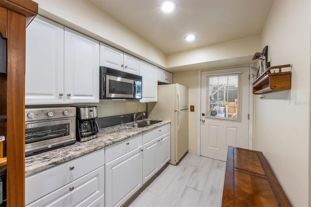 kitchen with light stone countertops, light wood-type flooring, sink, white fridge, and white cabinetry