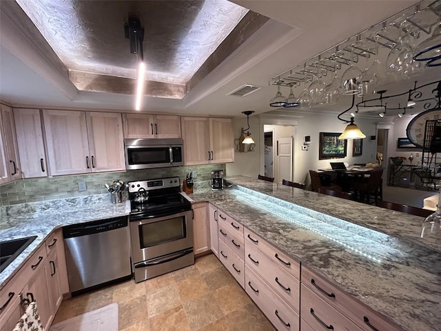 kitchen with hanging light fixtures, stainless steel appliances, a raised ceiling, tasteful backsplash, and light brown cabinetry