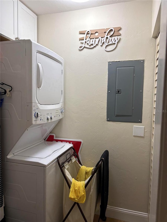 laundry room featuring stacked washer / drying machine, cabinets, and electric panel