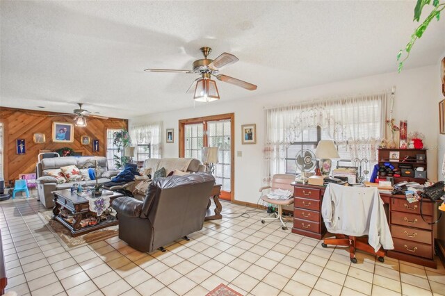 tiled living room featuring wood walls, ceiling fan, and a textured ceiling