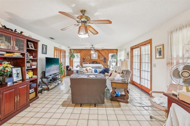 living room featuring french doors, a textured ceiling, light tile patterned floors, and wooden walls