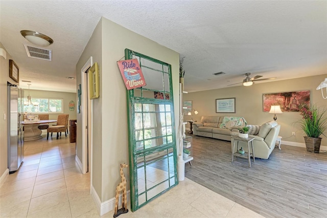 living room with ceiling fan, light wood-type flooring, and a textured ceiling