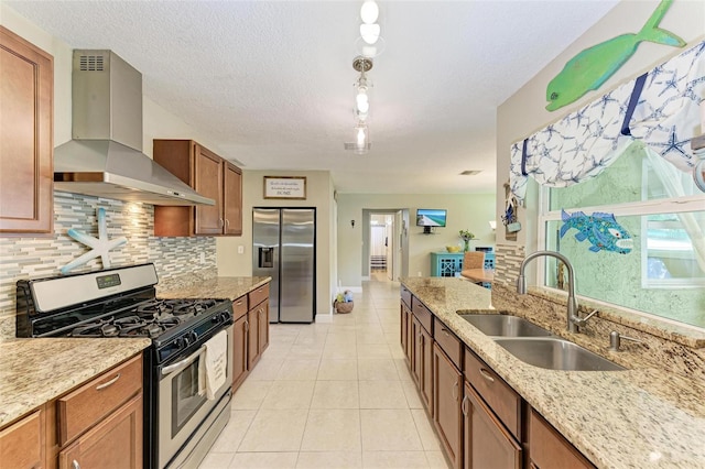 kitchen featuring wall chimney range hood, sink, a textured ceiling, light stone counters, and stainless steel appliances