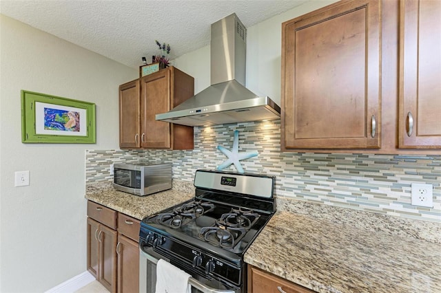 kitchen with wall chimney exhaust hood, decorative backsplash, light stone countertops, a textured ceiling, and stainless steel appliances