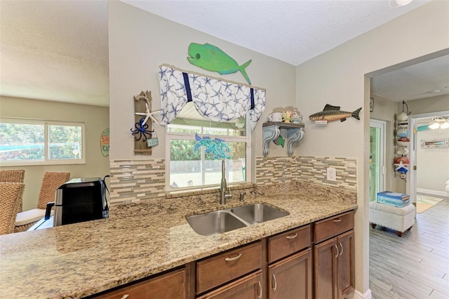 kitchen with light wood finished floors, a textured ceiling, a sink, backsplash, and light stone counters