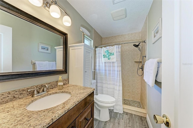 full bathroom with toilet, vanity, wood finished floors, and tiled shower