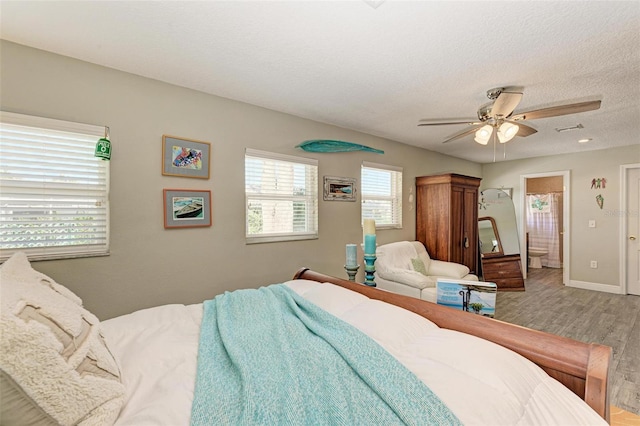 bedroom featuring wood finished floors, visible vents, a ceiling fan, connected bathroom, and a textured ceiling
