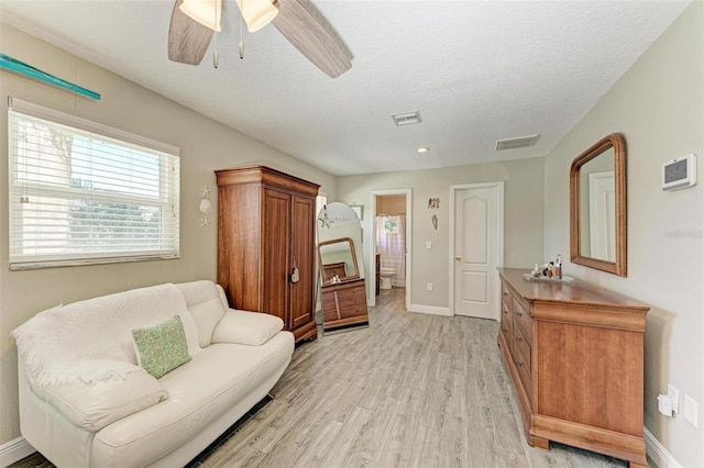 living area with ceiling fan, light wood finished floors, a textured ceiling, and visible vents