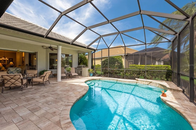 view of pool with a lanai, a patio area, ceiling fan, and an outdoor kitchen