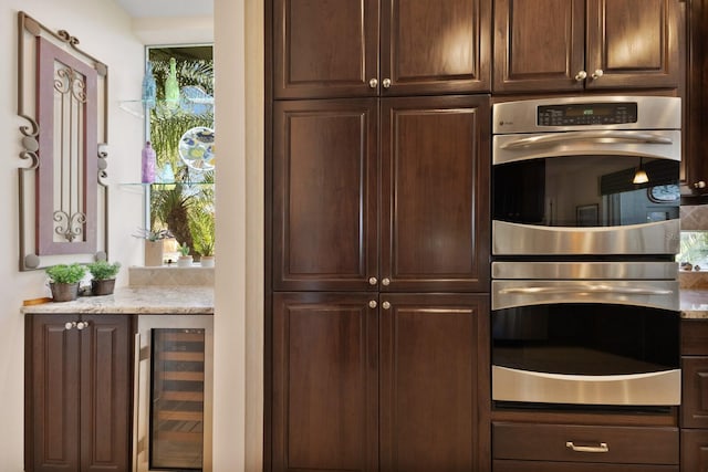 kitchen with plenty of natural light, dark brown cabinetry, stainless steel double oven, and wine cooler