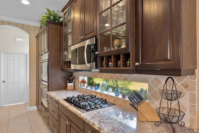 kitchen with ornamental molding, tasteful backsplash, dark brown cabinets, light stone counters, and stainless steel appliances