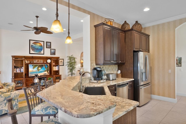 kitchen with kitchen peninsula, light stone counters, dark brown cabinetry, stainless steel appliances, and sink