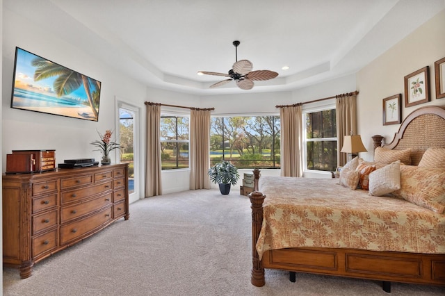 bedroom with a tray ceiling, multiple windows, light colored carpet, and ceiling fan