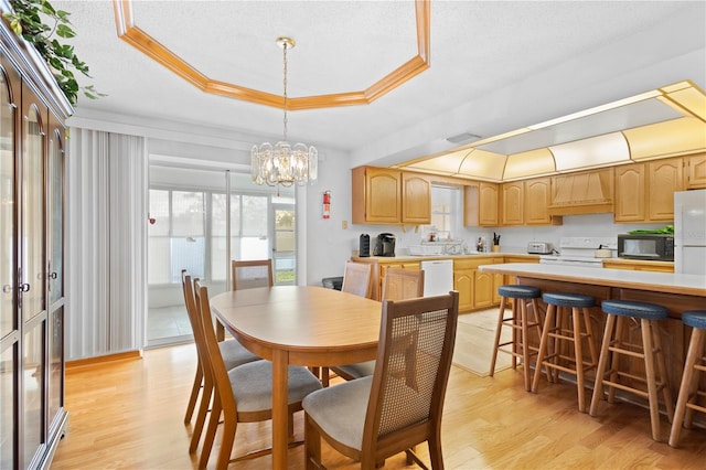 dining room featuring light wood-type flooring, an inviting chandelier, a wealth of natural light, and a raised ceiling