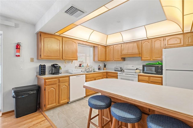 kitchen with light tile patterned floors, a breakfast bar area, white appliances, custom range hood, and sink