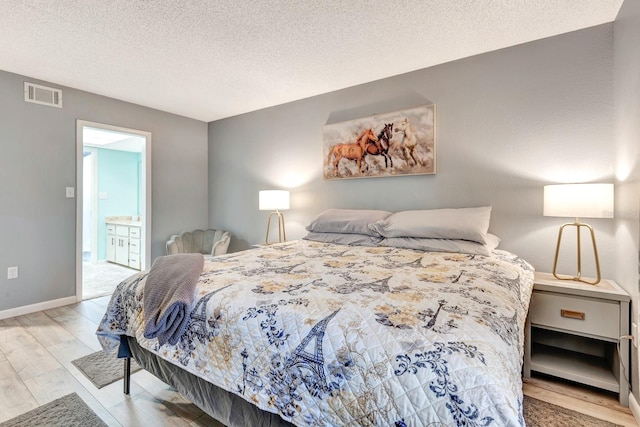 bedroom with ensuite bath, a textured ceiling, and light hardwood / wood-style flooring