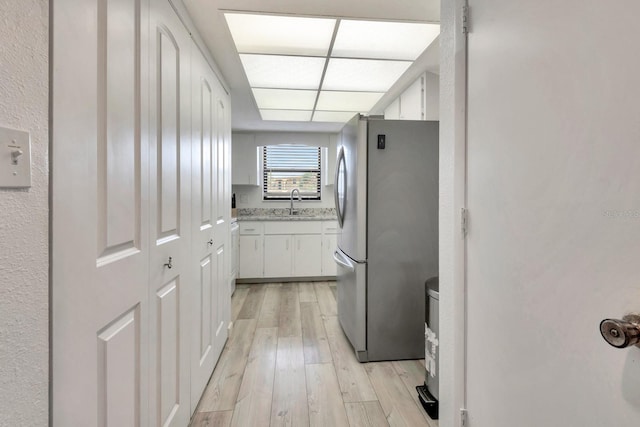 kitchen featuring sink, stainless steel fridge, white cabinets, and light wood-type flooring