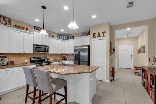 kitchen with appliances with stainless steel finishes, sink, dark stone counters, and an island with sink