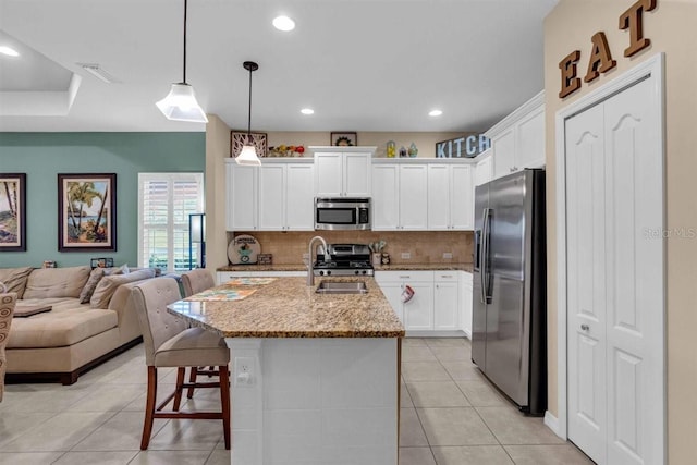 kitchen with appliances with stainless steel finishes, a kitchen breakfast bar, light stone counters, decorative light fixtures, and an island with sink