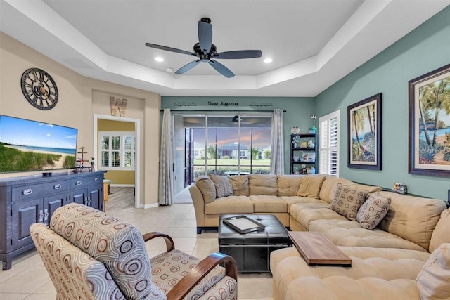 living room featuring a tray ceiling, ceiling fan, and light tile patterned floors