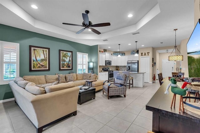 living room featuring a raised ceiling, ceiling fan, plenty of natural light, and light tile patterned floors