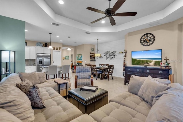 living room with ceiling fan, a raised ceiling, and light tile patterned floors