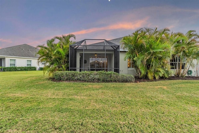 back house at dusk featuring a lanai and a lawn