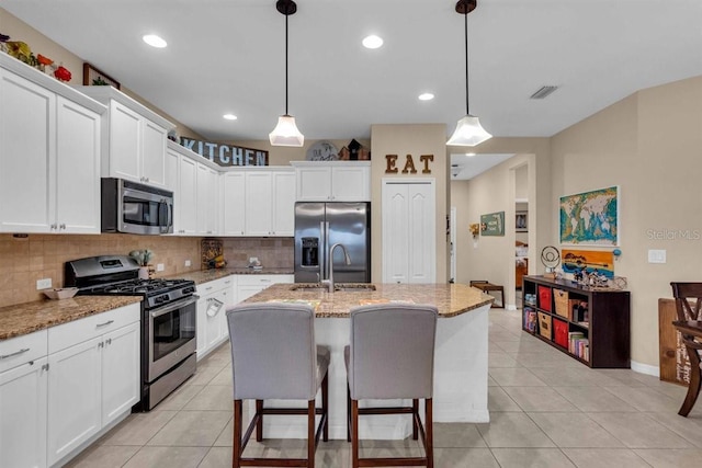 kitchen featuring appliances with stainless steel finishes, decorative light fixtures, light stone counters, and an island with sink