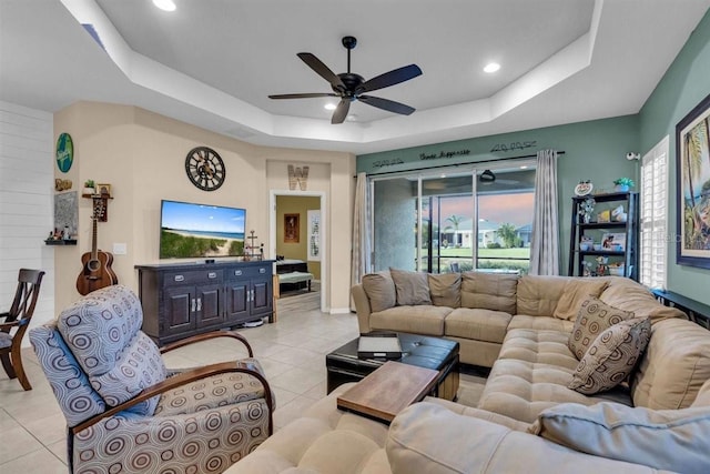 tiled living room with ceiling fan and a tray ceiling