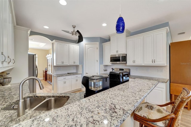 kitchen with white cabinets, hanging light fixtures, sink, light hardwood / wood-style flooring, and appliances with stainless steel finishes