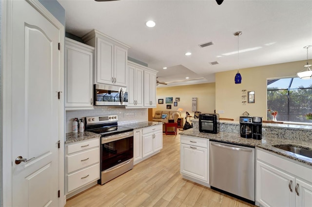 kitchen with light stone counters, stainless steel appliances, light hardwood / wood-style flooring, white cabinets, and hanging light fixtures