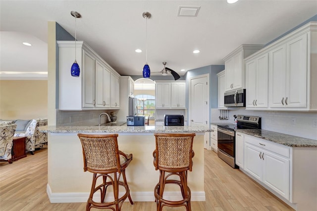 kitchen featuring kitchen peninsula, hanging light fixtures, stainless steel appliances, and light wood-type flooring