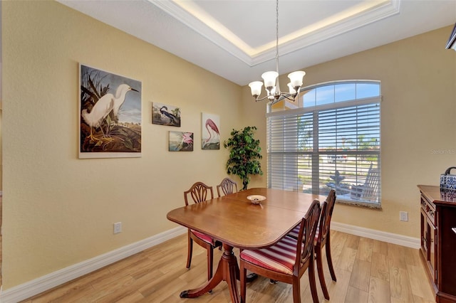 dining space featuring an inviting chandelier, light hardwood / wood-style flooring, and a tray ceiling