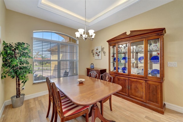 dining room with a raised ceiling, an inviting chandelier, and light wood-type flooring