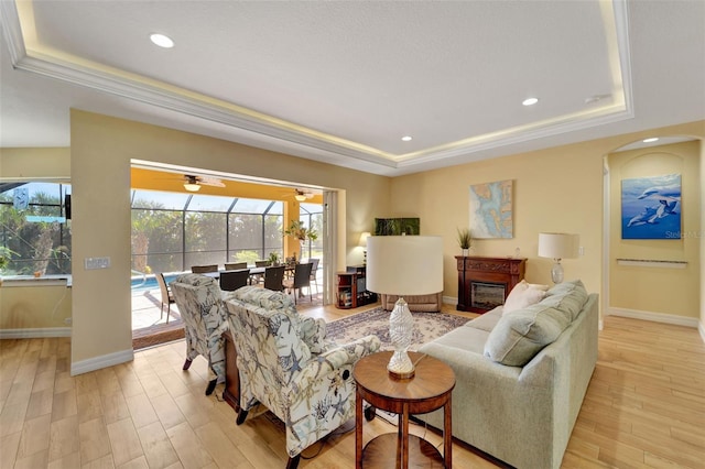 living room featuring ceiling fan, a raised ceiling, crown molding, and light hardwood / wood-style flooring