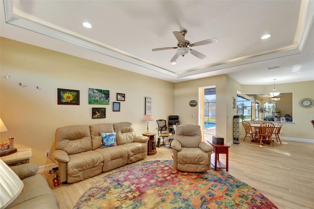 living room with ceiling fan, light hardwood / wood-style floors, a raised ceiling, and ornamental molding