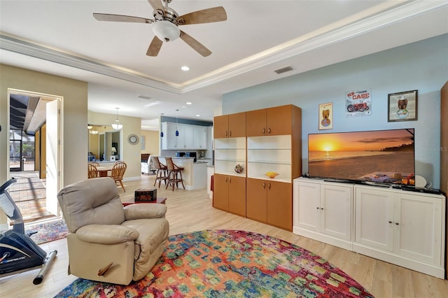 living room with ceiling fan, a tray ceiling, and light hardwood / wood-style flooring