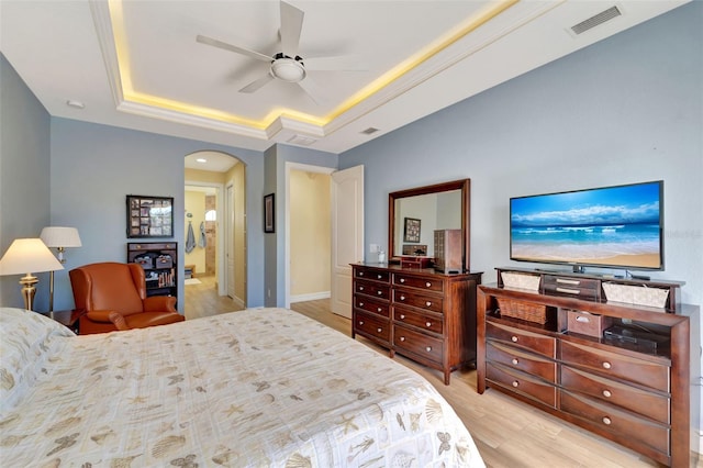 bedroom featuring ceiling fan, a raised ceiling, ensuite bath, and light hardwood / wood-style flooring