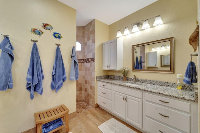 bathroom featuring a tile shower, vanity, and wood-type flooring