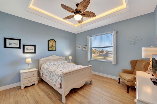 bedroom with ceiling fan, light hardwood / wood-style flooring, and a tray ceiling