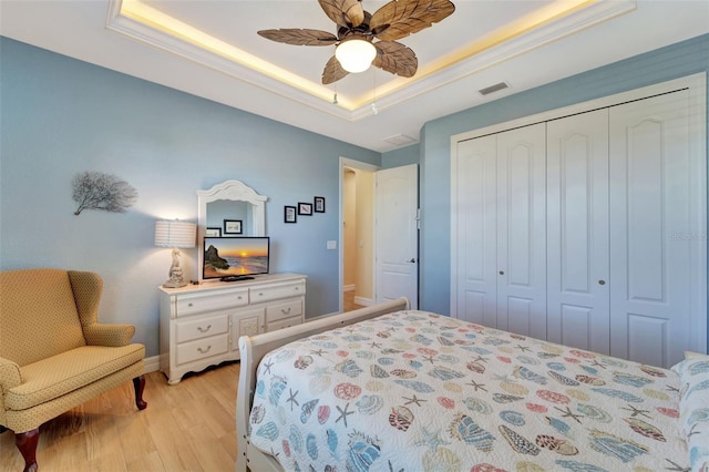 bedroom with ceiling fan, a closet, a raised ceiling, and light hardwood / wood-style flooring