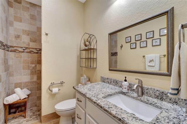 bathroom with toilet, vanity, hardwood / wood-style floors, and tiled shower