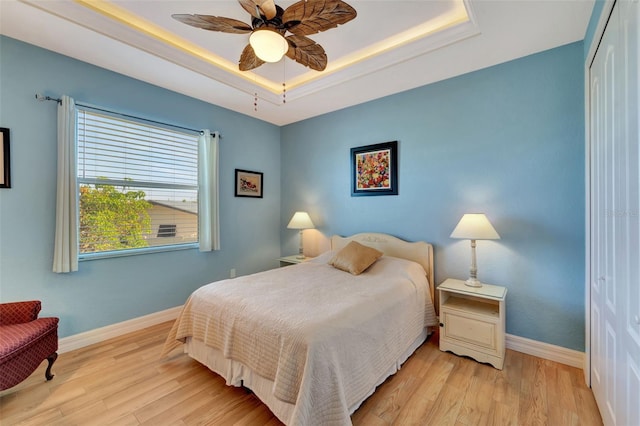 bedroom featuring a tray ceiling, a closet, ceiling fan, and light hardwood / wood-style flooring