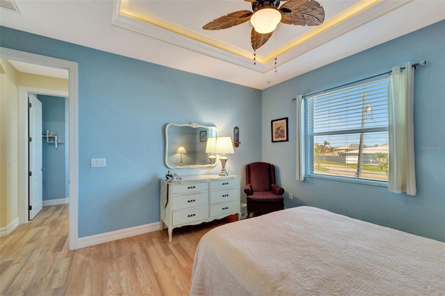 bedroom with ceiling fan, light hardwood / wood-style flooring, and a tray ceiling