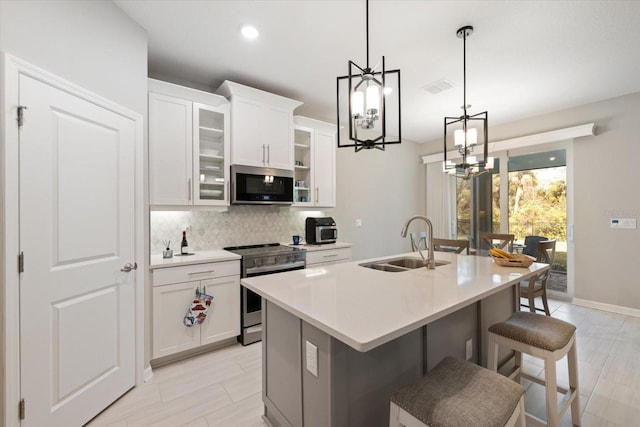 kitchen featuring stainless steel appliances, sink, white cabinets, a breakfast bar area, and an island with sink