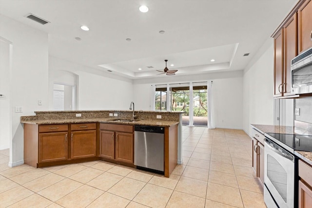 kitchen featuring ceiling fan, sink, stainless steel appliances, a raised ceiling, and stone countertops