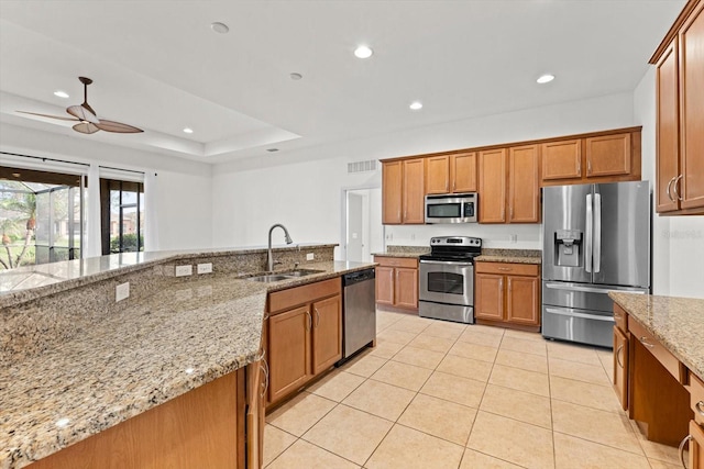 kitchen with light stone countertops, sink, ceiling fan, stainless steel appliances, and a raised ceiling