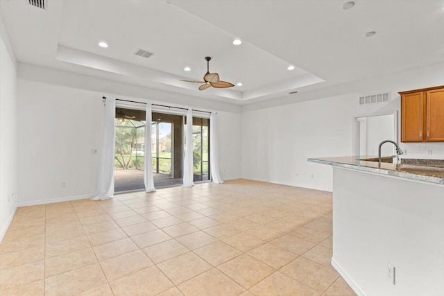 unfurnished living room featuring a raised ceiling, ceiling fan, and light tile patterned floors